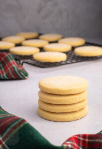 Stack of round Scottish shortbread biscuits with more cooling on a wire rack.