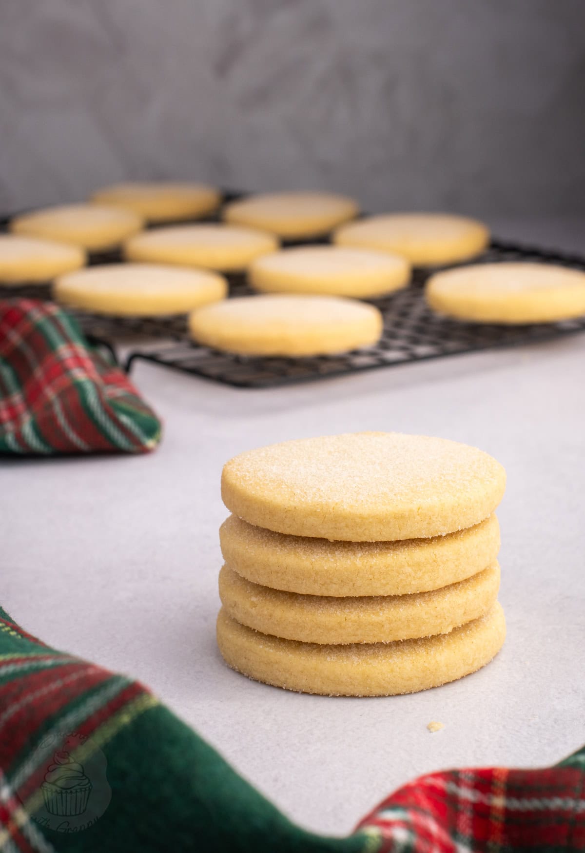 Stack of round Scottish shortbread biscuits with more cooling on a wire rack.