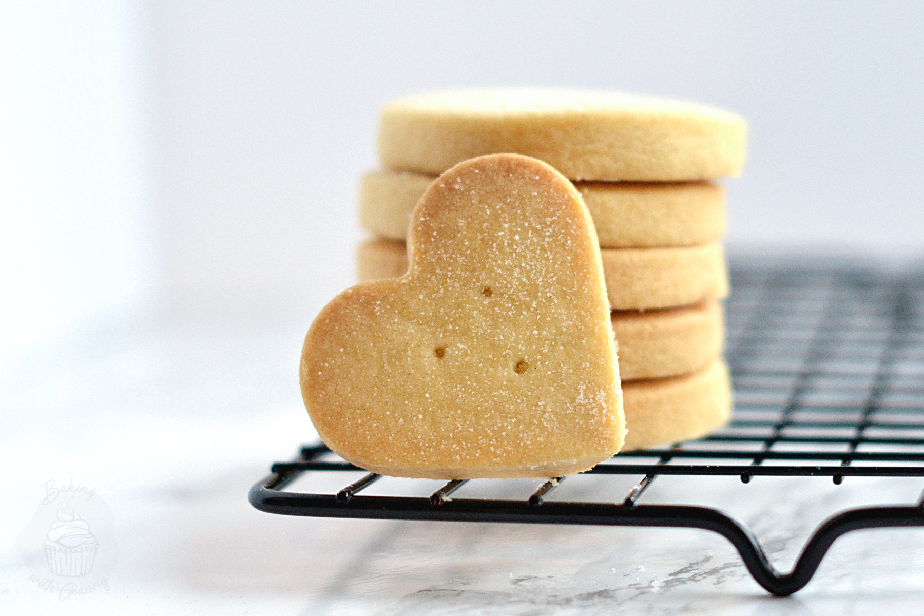 Heart-shaped shortbread biscuit in front of a stack of round shortbread.