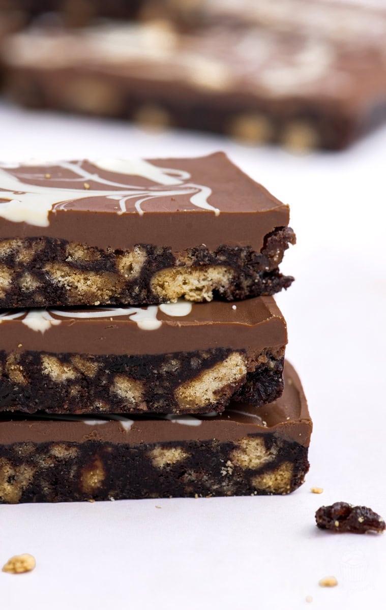 Close-up of three stacked slices of Scottish chocolate tiffin, showing biscuit pieces and a smooth chocolate topping with white chocolate swirls.