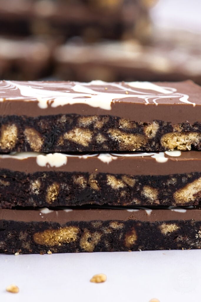 Side view of three chocolate tiffin bars with a marbled chocolate top and visible biscuit chunks in the dense base.
