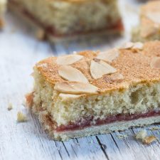 Almond Slice close-ip, showing the pastry bottom, raspberry jam filling and almond sponge, topped with flaked almonds.