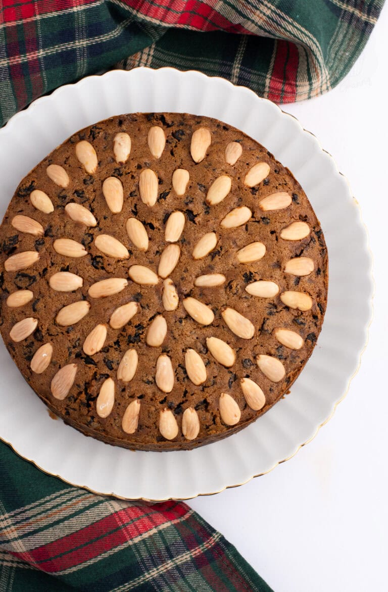 Traditional Scottish Dundee Cake, with almond topping, packed with rich dried fruit. On a white plate, atop a tartan fabric.