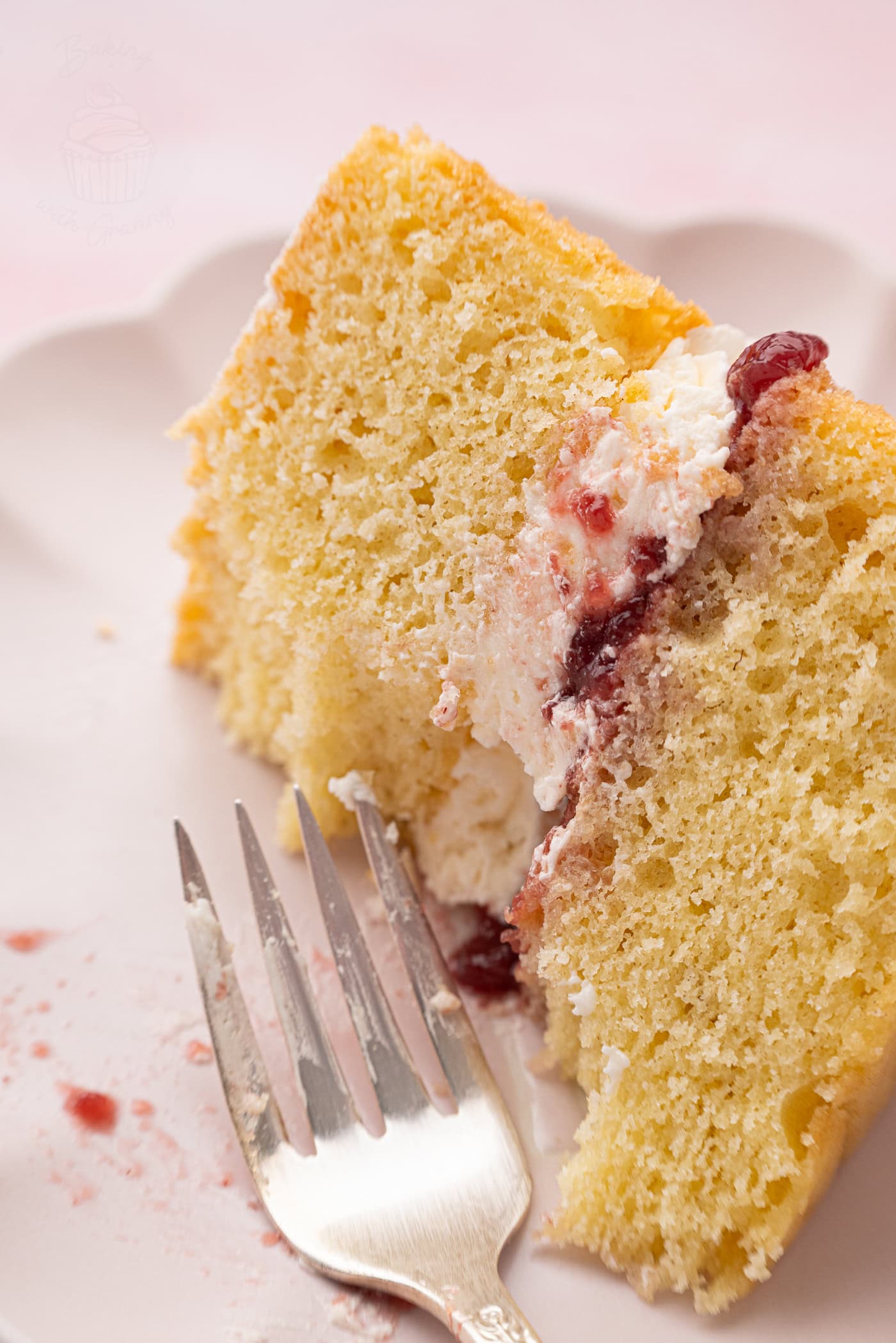 Close-up of a single bite of Victoria Sponge cake on a fork, showing the airy sponge and rich jam and cream centre.