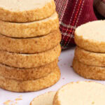 Stack of Highlander Shortbread biscuits coated in demerara sugar, with a tartan cloth in the background.