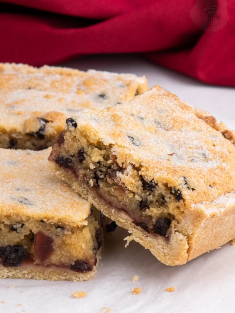 Close-up of a sliced Paradise Slice with a crumbly golden top, currants, cherries, and jam filling.
