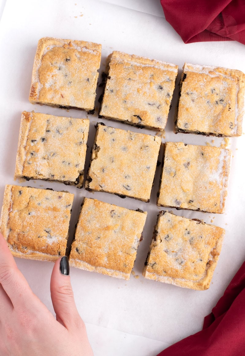 Hand reaching for a square of Paradise Slice from a batch of nine dusted with sugar.