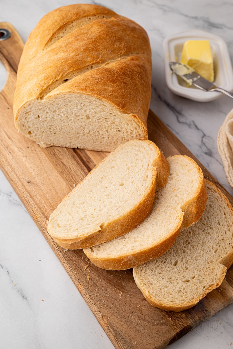 Freshly baked white loaf sliced on a wooden board with butter nearby.