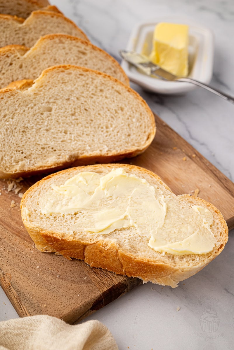 Slice of homemade white bread spread with butter on a wooden board.