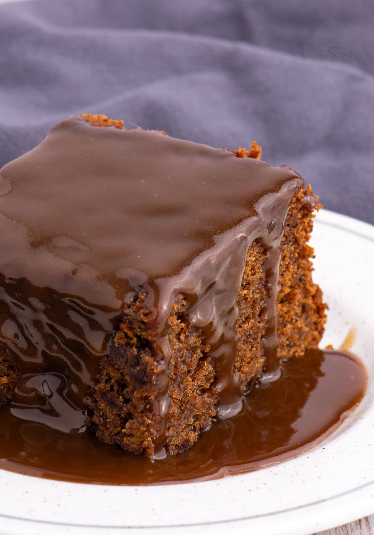 Close-up of sticky toffee pudding topped with rich toffee sauce, dripping down the sides of the moist sponge.