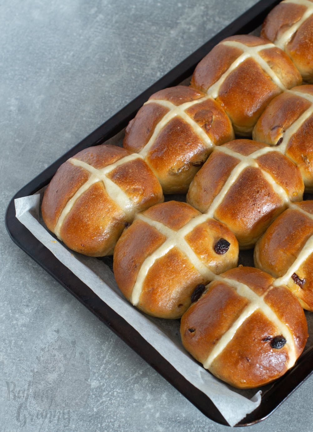Freshly baked hot cross buns in tray with golden tops and traditional cross.