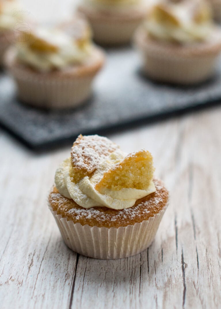 Individual butterfly cake with buttercream and sponge wings, with more cakes softly blurred in the background.