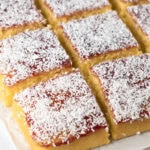 Close-up of a slice of old school cake on baking paper, with golden sponge, vibrant jam, and coconut.
