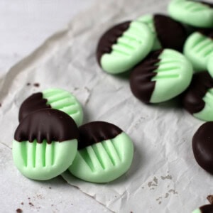 Mint green peppermint creams partially dipped in chocolate are arranged on crinkled parchment paper. These peppermint creams boast a ridged pattern achieved by pressing with a fork, adding texture to their smooth surface