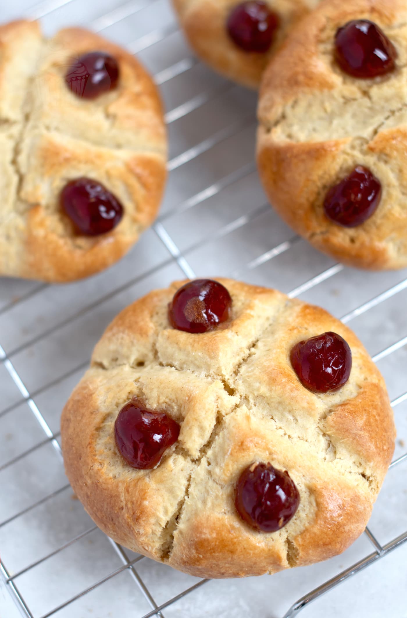 Freshly baked Victoria Scones, cooling on a wire rack. Finished with a cross over the top, with 4 glace cherry halves that look like jewels on a crown.