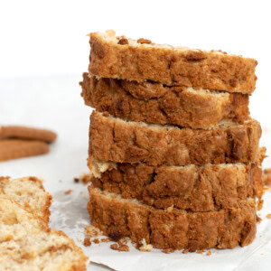 Slices of Banana Biscoff bread, stacked on top of each other, with a couple of extra slices to the side and some Biscoff biscuits in the background.