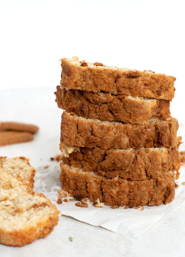 Slices of Banana Biscoff bread, stacked on top of each other, with a couple of extra slices to the side and some Biscoff biscuits in the background.