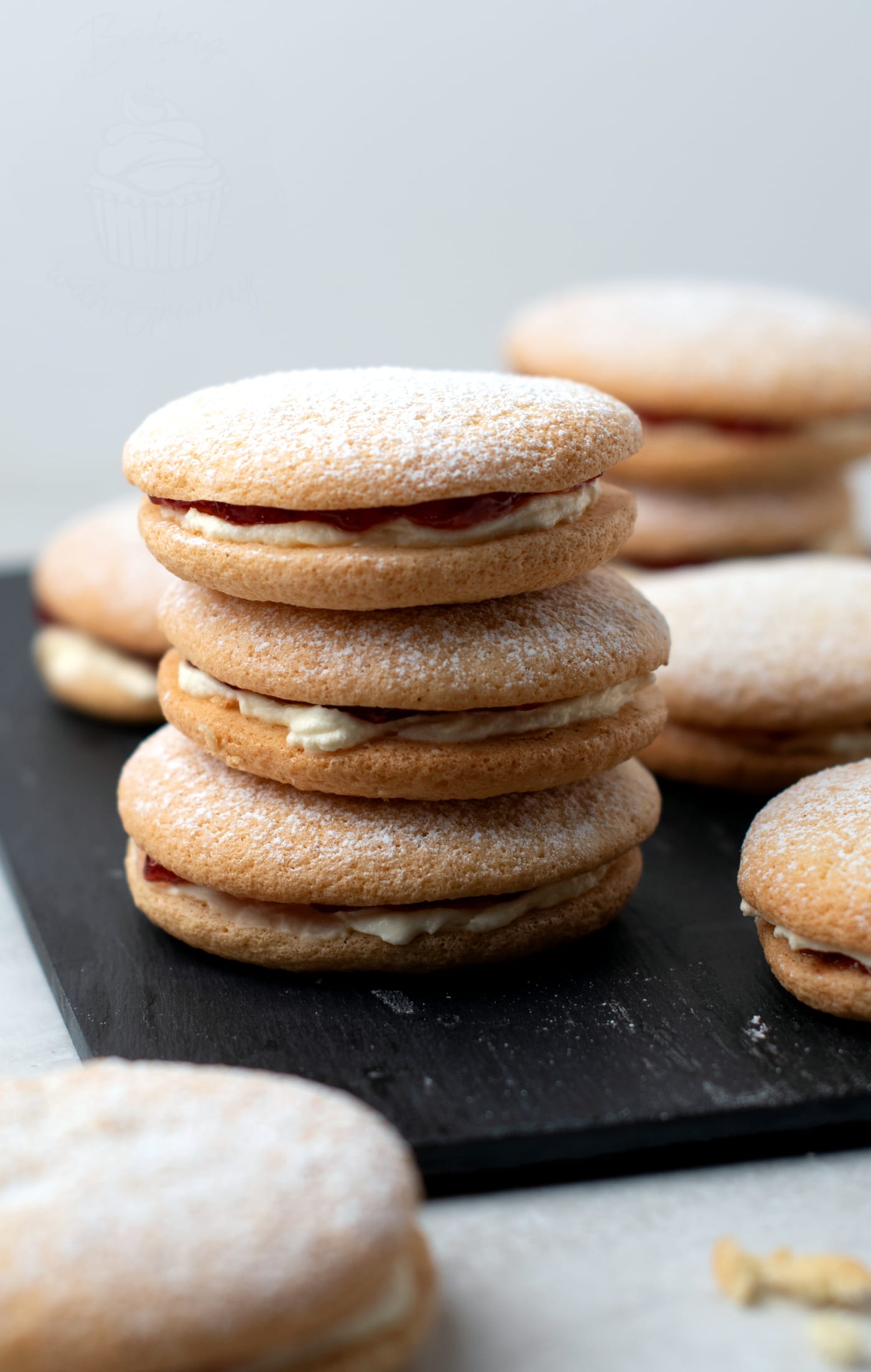 A batch of finished vanilla Sponge Drops, filled with jam and cream, and topped with a dusting of sugar.