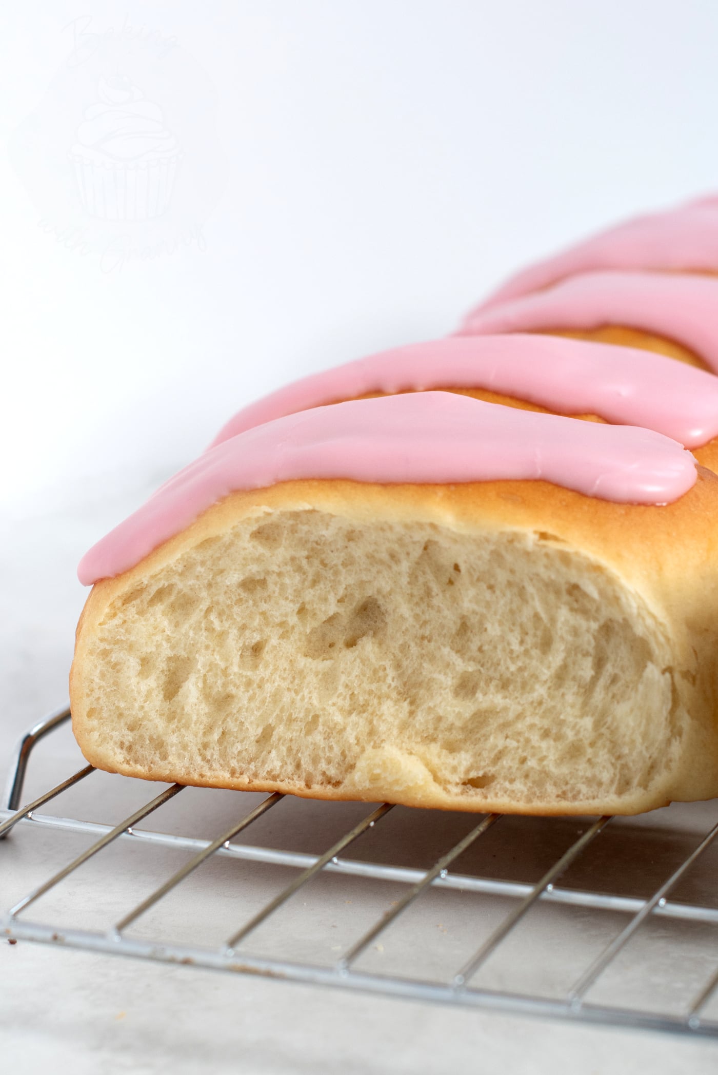 Close up of an Iced Finger Bun. Soft doughy bun, topped with sticky pink icing.