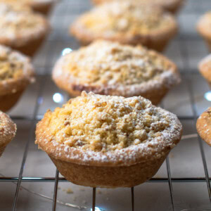 Crumble Top Mince Pies recipe from Baking with Granny. Delicious classic shortcrust mince pie, with a crumble topping, sat on top of a cooling rack, with Christmas lights twinkling underneath.