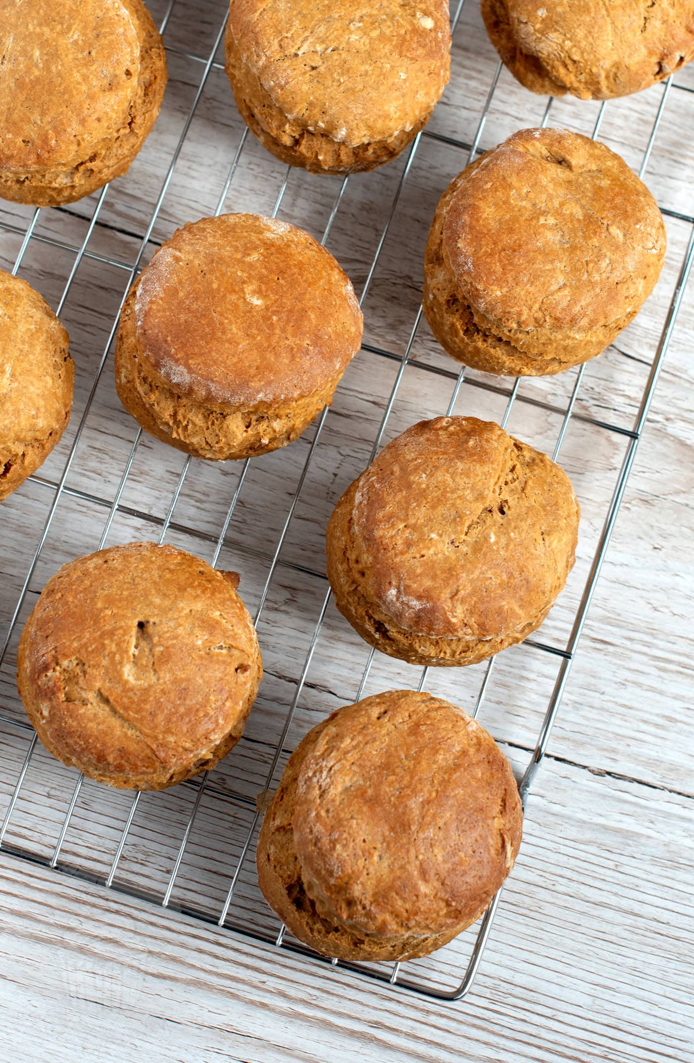 Freshly baked treacle scones cooling on a wire rack, placed on a light wooden surface. The scones are golden brown and evenly spaced out.