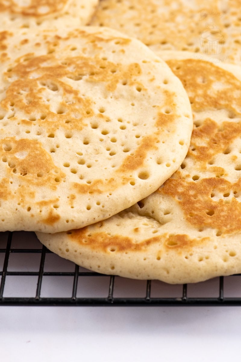 Homemade British crumpets resting on a cooling rack after cooking.