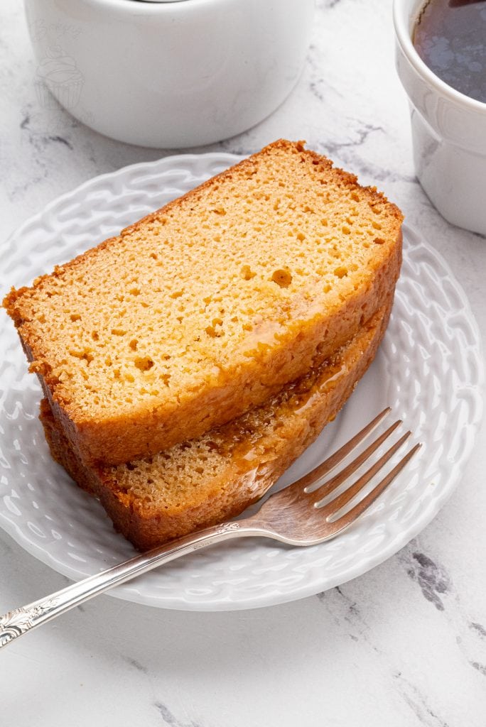 Two slices of golden syrup cake on a white plate with coffee cups.