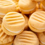 Close-up of custard cream biscuits stacked together, showing creamy filling between two golden biscuits