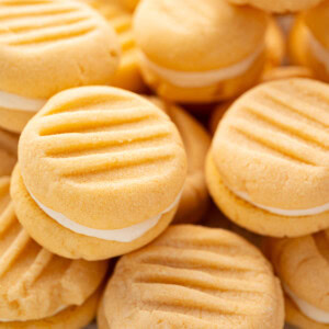Close-up of custard cream biscuits stacked together, showing creamy filling between two golden biscuits