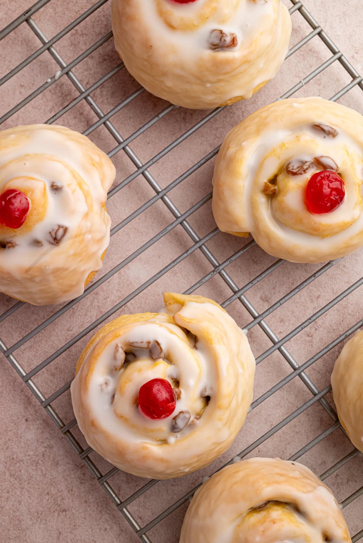 Overhead view of Belgian buns cooling on a wire rack, all topped with white icing and glacé cherries.