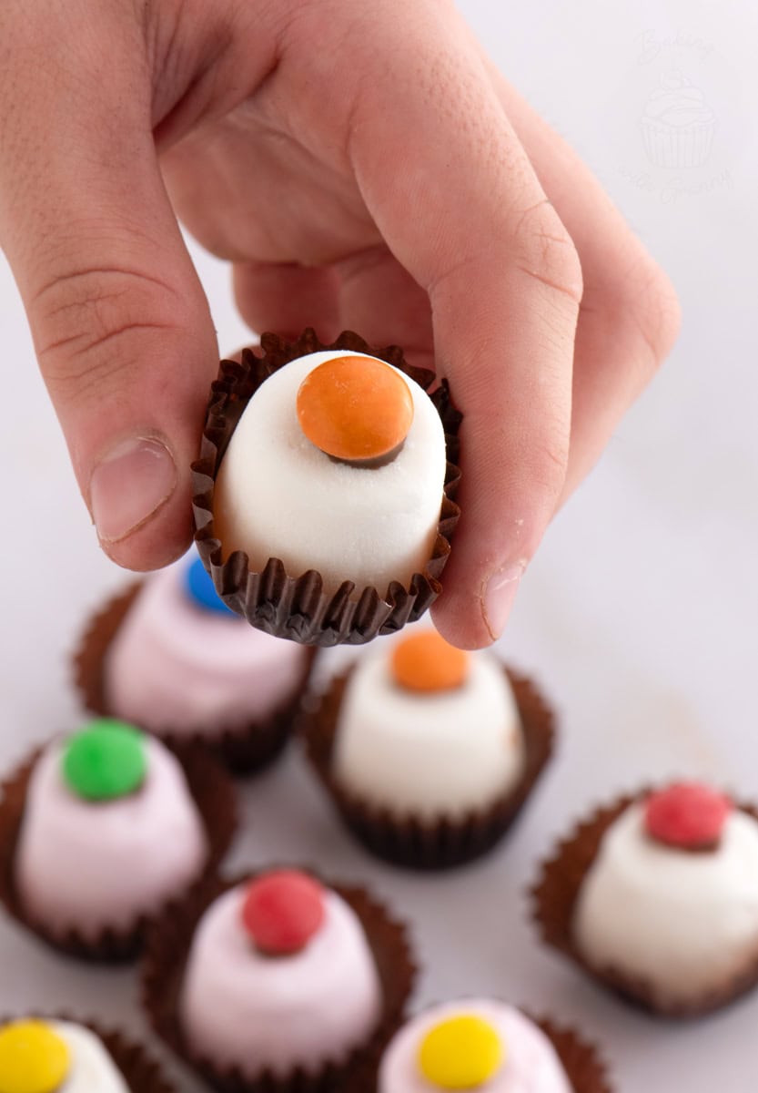 Child’s hand holding a Marshmallow Top Hat with white marshmallow and orange smartie topping.