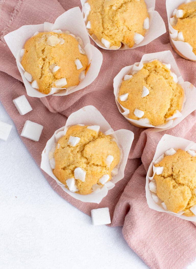 Freshly baked Sair Heidies fairy cakes in tulip muffin cases, decorated with broken sugar cubes on top, sitting on a pink cloth.