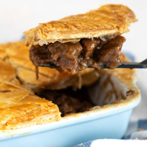 Slice of Scottish steak pie being lifted from the dish, showing chunks of beef in thick gravy.