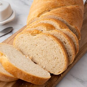 Freshly baked white bread sliced on a wooden board with butter nearby.