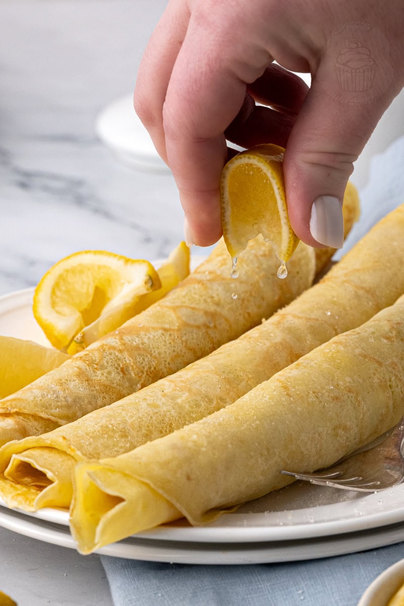 Hand squeezing fresh lemon juice over classic British pancakes dusted with sugar.