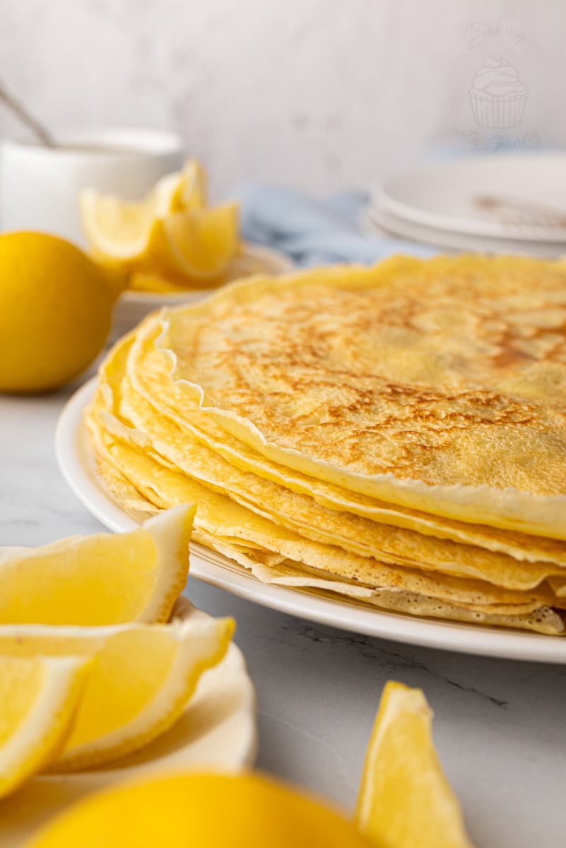 Side view of freshly cooked English pancakes stacked on a white plate.