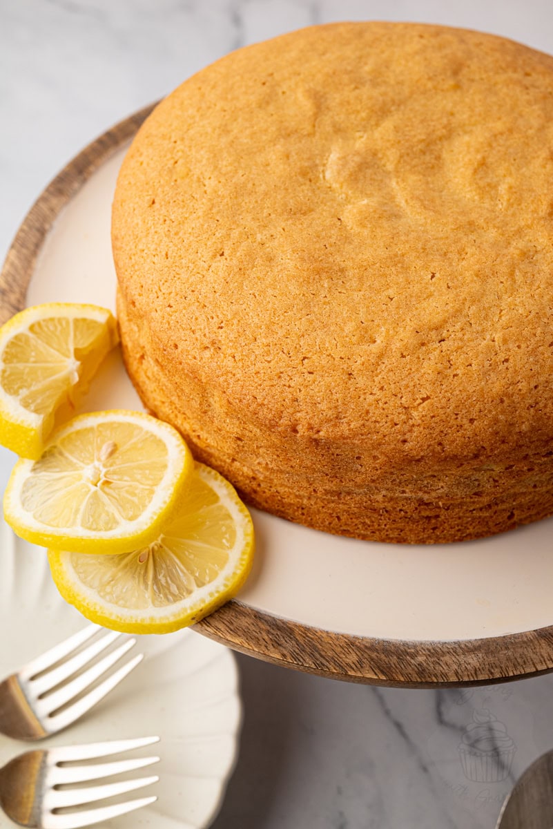 Golden Madeira cake on a cake stand styled with sliced lemons on a marble surface.