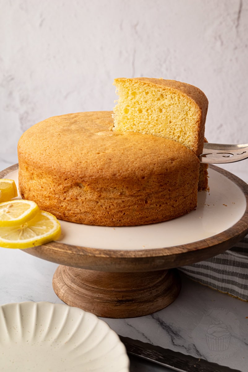 Classic Madeira cake on a cake stand with one slice removed, styled with fresh lemon slices.