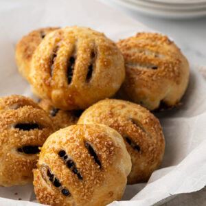 Golden brown Eccles cakes with sugar topping on baking paper.