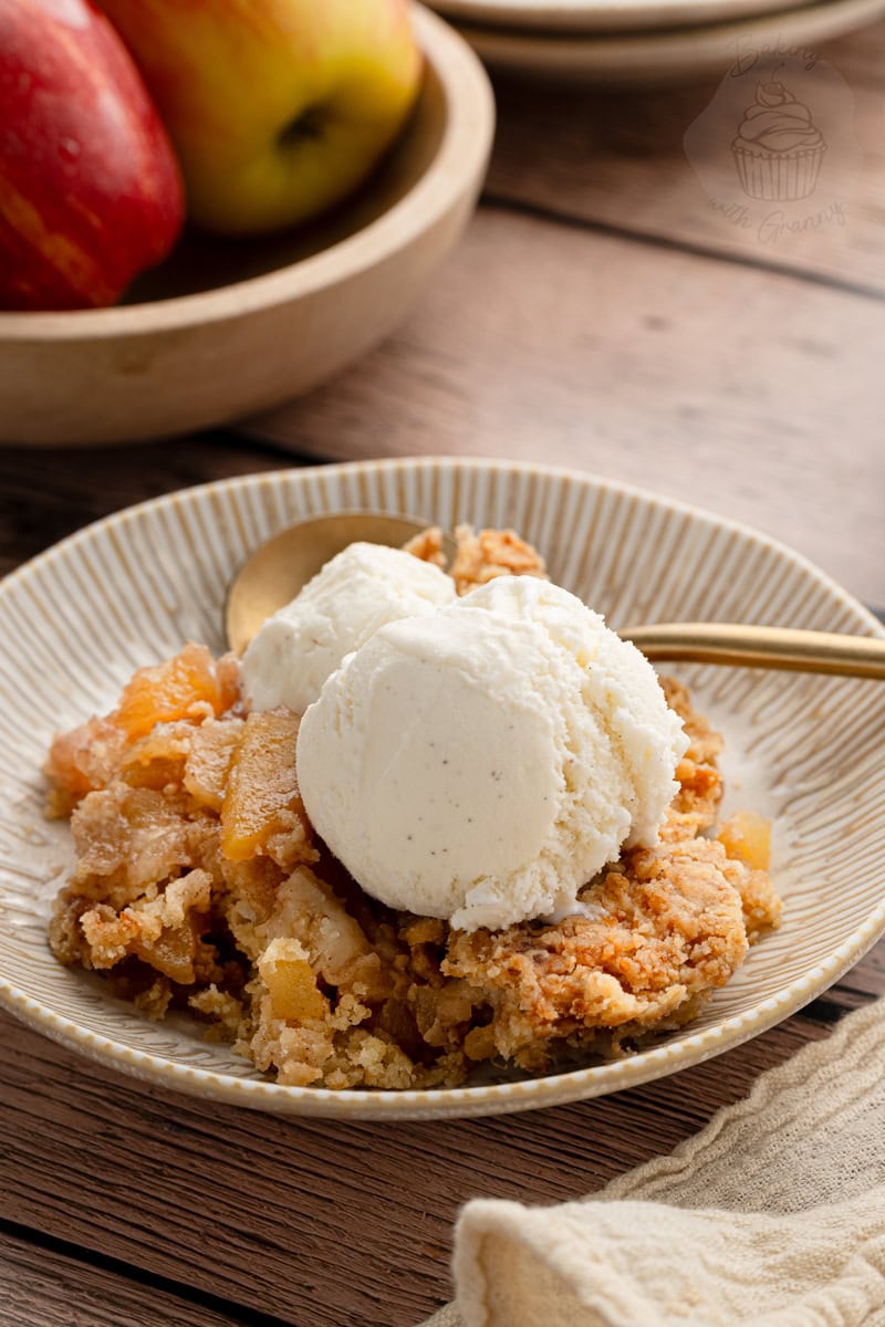 A scoop of vanilla bean ice cream melting over a fresh serving of cinnamon apple crumble on a rustic wooden background.
