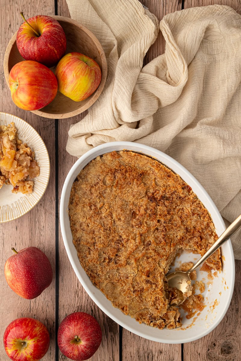 A classic British apple crumble recipe served from an oval baking dish, showcasing a golden brown flour and butter streusel topping.