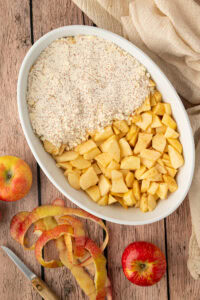 An overhead view showing the process of making apple crumble without oats, with flour streusel topping being layered over chopped baking apples.