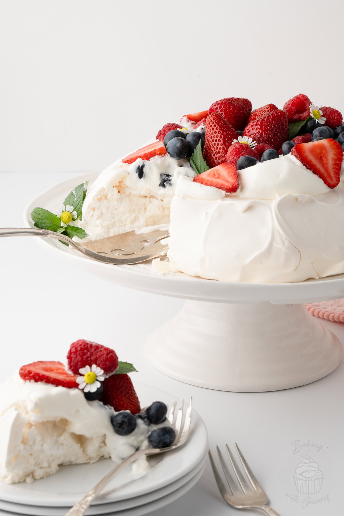 Berry Pavlova on a cake stand with a slice served on a plate.