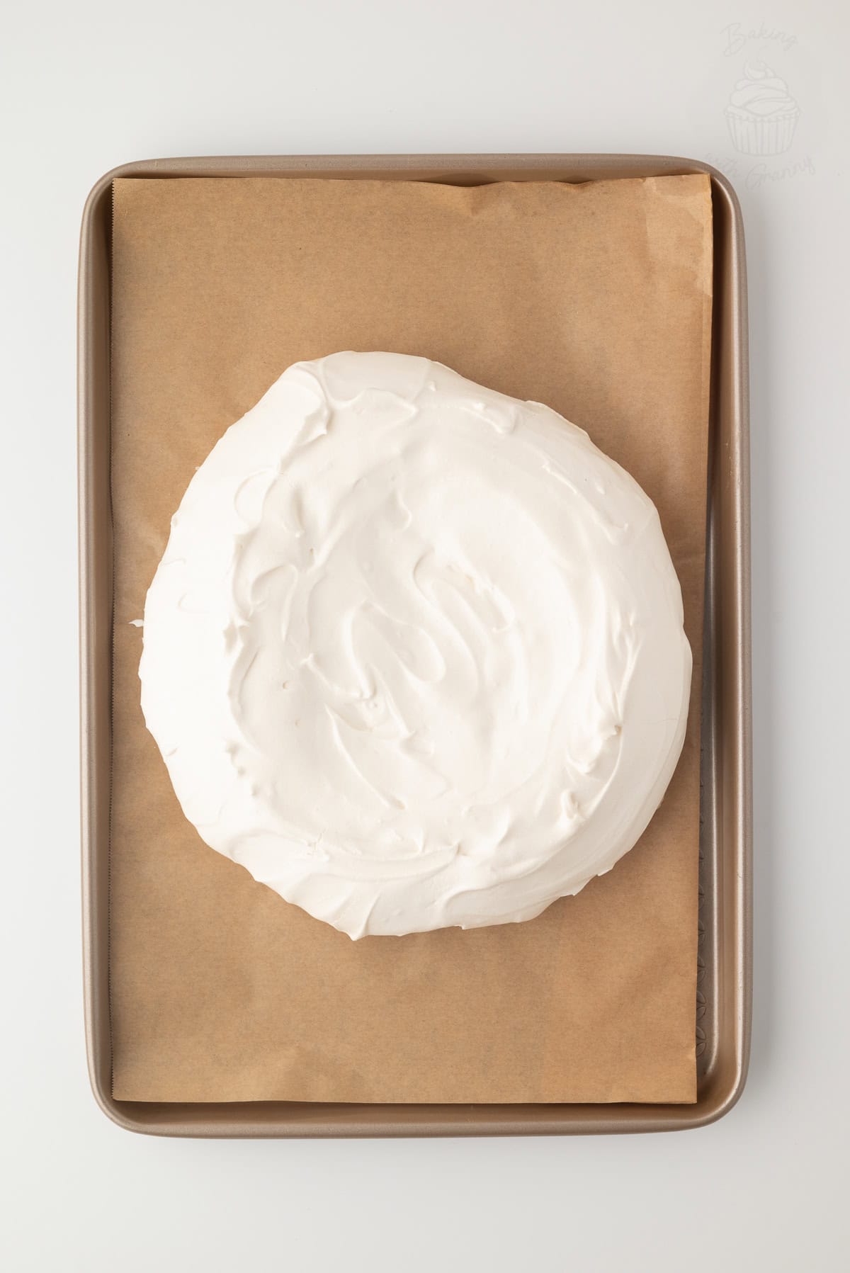 Baked Pavlova meringue shaped into a round on a lined baking tray.