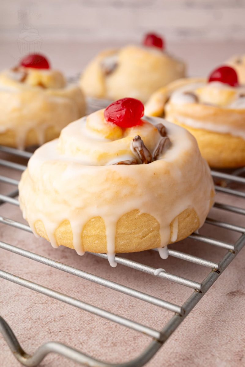Belgian Buns Iced Belgian buns with glacé cherries cooling on a rack, showing the golden bake and soft texture of the buns.