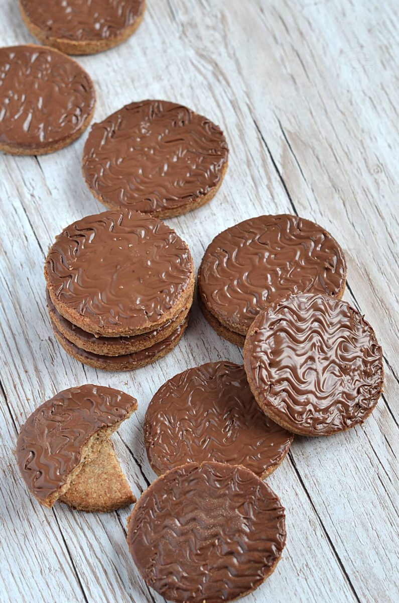 Chocolate Digestive A row of homemade chocolate digestive biscuits on a rustic wooden surface, with one cookie partially eaten to show the crisp, crumbly texture.