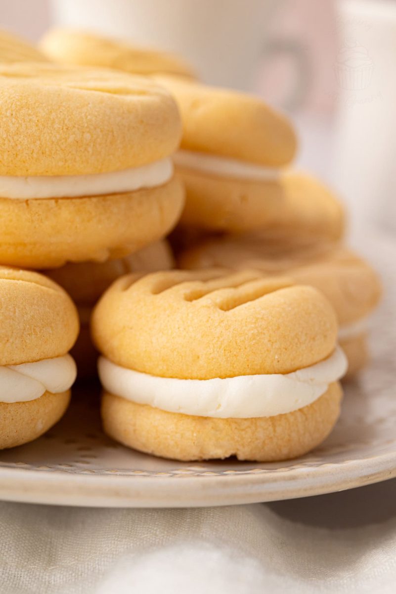 Custard Creams Tightly framed view of custard cream cookies stacked on a plate, showing ridged tops and thick filling.