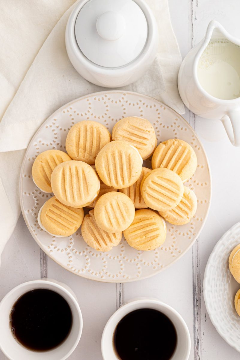 Custard Creams Top-down view of a full plate of custard creams served with cups of coffee and milk jug.