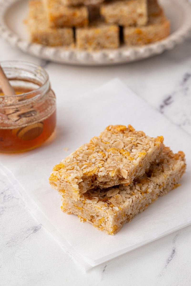 Two slices of honey slice stacked on white parchment paper with a jar of honey and a honey dipper in the background.