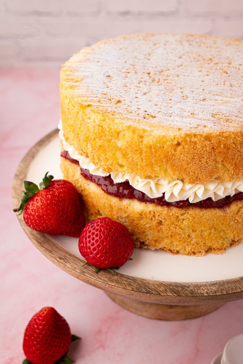 Victoria Sponge Close-up of a Victoria Sponge cake with visible layers of piped buttercream and jam, alongside whole strawberries on the cake stand.